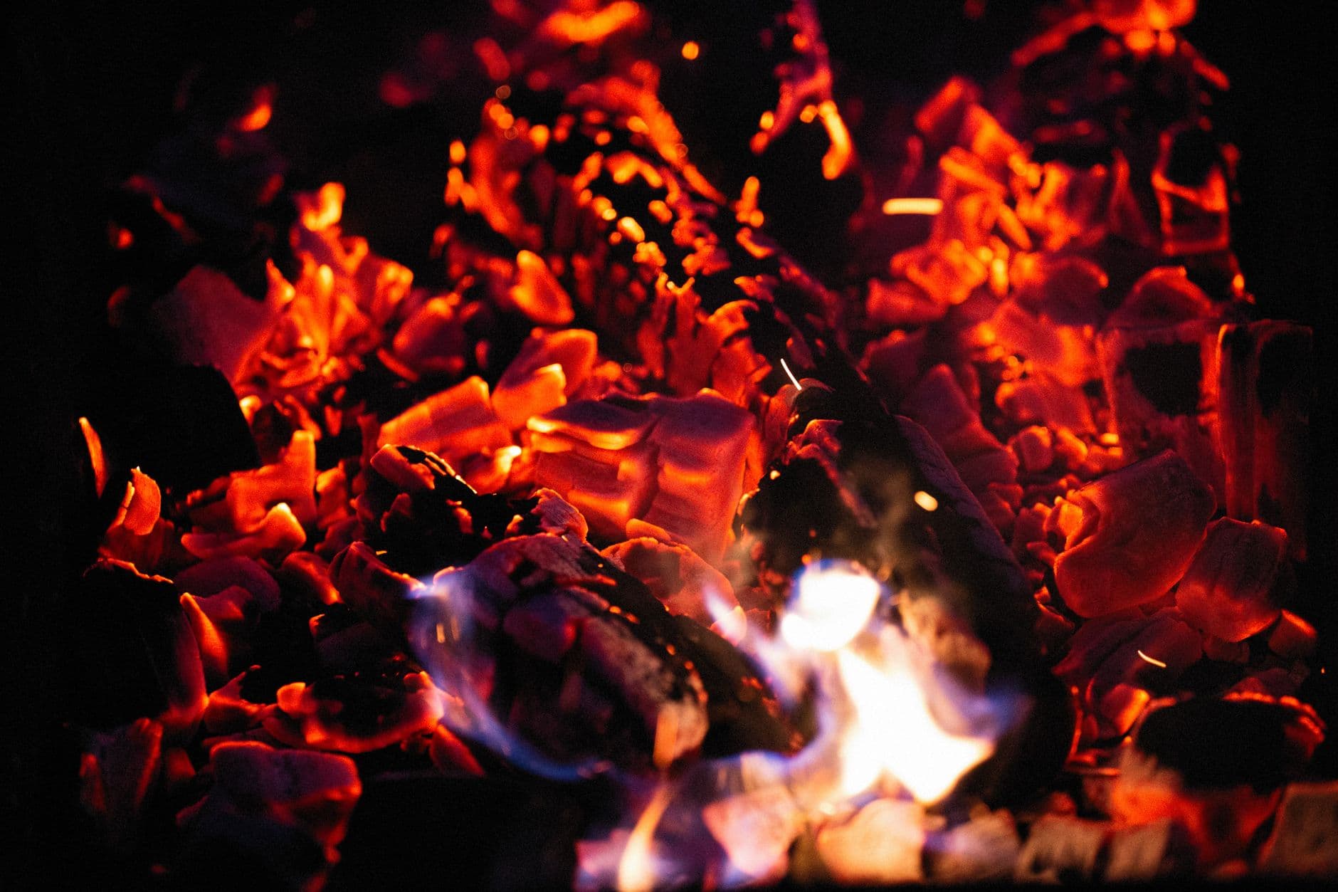 An intense close-up of glowing hot coals and vibrant flames at night, creating a fiery spectacle.